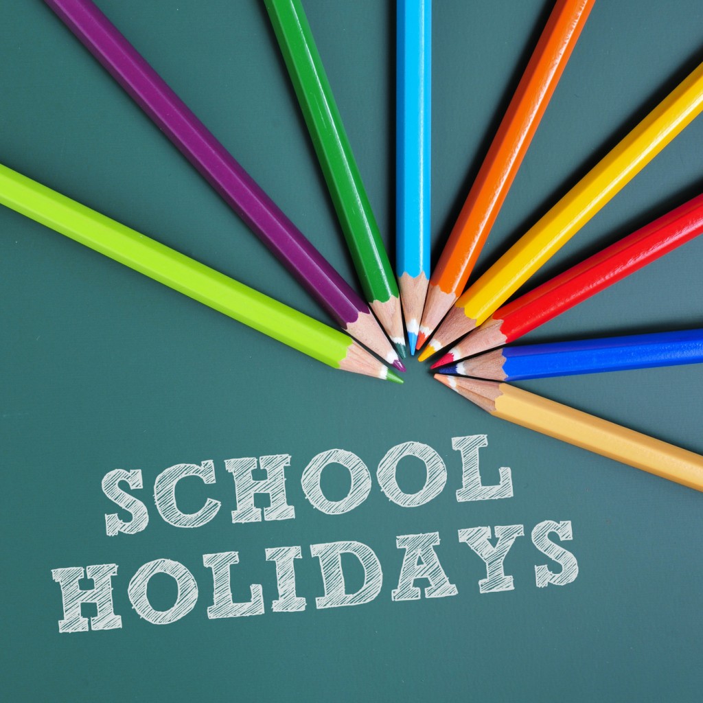 coloured pencils of different colors and text school holidays writtten in a green chalkboard